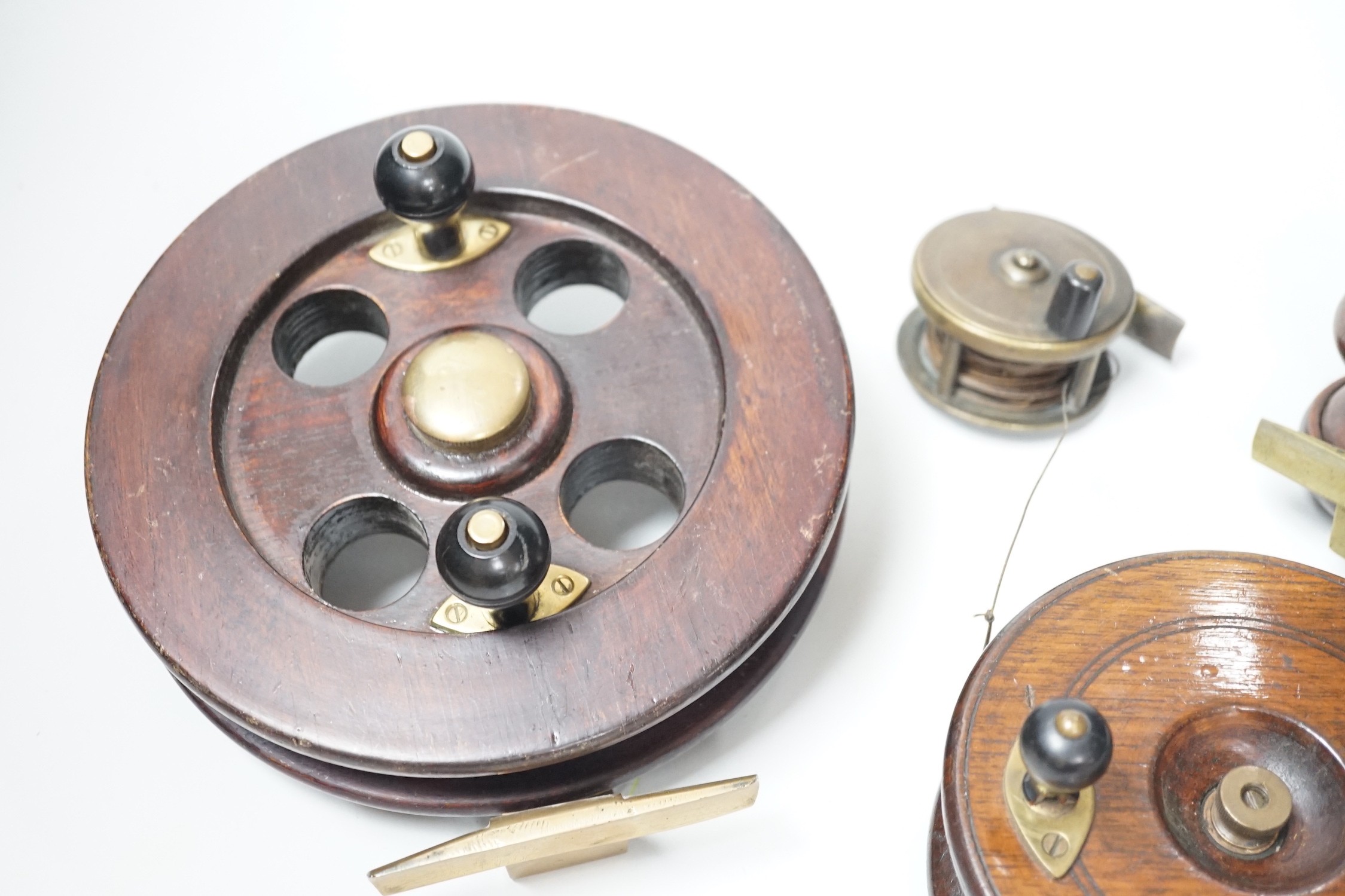 Three mahogany and brass fishing reels, largest 19 cm diameter and an Army & Navy brass reel, 6.3cm diameter